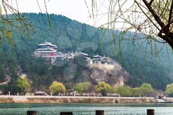 travel to China - green tree on waterfront Yi river and blurred East Hill of Chinese Buddhist monument Longmen Grottoes (Dragon's Gate Grottoes, Longmen Caves) on background in spring season