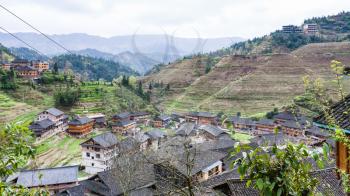 travel to China - above view of Dazhai village in mountain valley on green hills in area Longsheng Rice Terraces (Longji Rice Terraces) in spring