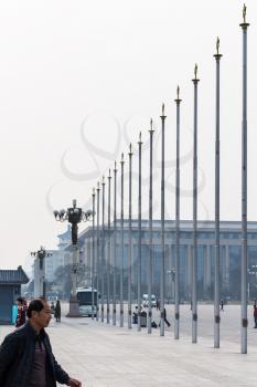 BEIJING, CHINA - MARCH 19, 2017: tourists near flagpoles on Tiananmen Square and view of the building of Great hall of The people in spring. Tiananmen Square is central city square in Beijing