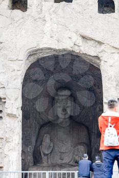 LUOYANG, CHINA - MARCH 20, 2017: visitors near Sakyamuni statue in Middle Binyang Cave in Longmen Grottoes (Longmen Caves). The complex was inscribed upon the UNESCO World Heritage List in 2000