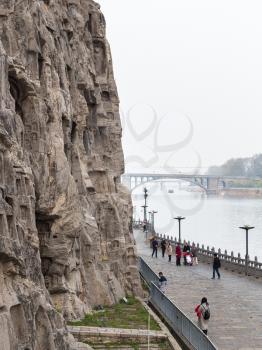 LUOYANG, CHINA - MARCH 20, 2017: view of people on waterfront and Bridge in Chinese Buddhist monument Longmen Grottoes. The complex was inscribed upon the UNESCO World Heritage List in 2000
