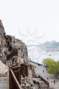 LUOYANG, CHINA - MARCH 20, 2017: view of tourists on quay and Bridge in Chinese Buddhist monument Longmen Grottoes. The complex was inscribed upon the UNESCO World Heritage List in 2000
