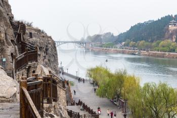 LUOYANG, CHINA - MARCH 20, 2017: view of tourists on embankment and Bridge in Chinese Buddhist monument Longmen Grottoes. The complex was inscribed upon the UNESCO World Heritage List in 2000