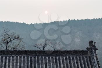 LUOYANG, CHINA - MARCH 20, 2017: sun over roof of temple on East Hill of Chinese Buddhist monument Longmen Grottoes in spring. The complex was inscribed upon the UNESCO World Heritage List in 2000