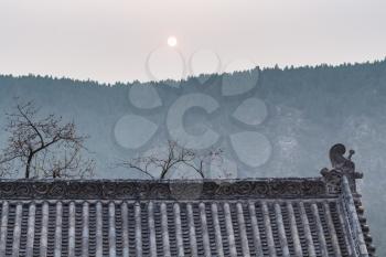 LUOYANG, CHINA - MARCH 20, 2017: sun over roof of pagoda on East Hill of Chinese Buddhist monument Longmen Grottoes in spring. The complex was inscribed upon the UNESCO World Heritage List in 2000