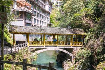 JIANGDI, CHINA - MARCH 26, 2017: tourists on bridge over gorge with creek near spa resort hotels in Longsheng Hot Springs National Forest Park of Xiangshan District in spring season