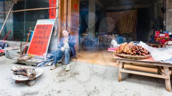 CHENGYANG, CHINA - MARCH 27, 2017: seller near local eatery and smokehouse in Chengyang village of Sanjiang Dong Autonomous County in spring. Chengyang includes eight villages of the Dong people