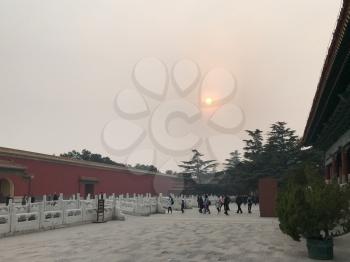 BEIJING, CHINA - MARCH 19, 2017: people near wall of gate in Imperial Ancestral Hall public park in Beijing Imperial city under sun in brown from smog sky in spring