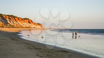 Travel to Algarve Portugal - people walk on beach Praia Falesia near Albufeira city during evening ebb