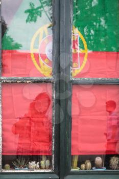 Travel to Algarve Portugal - The Flag of Portugal and reflection of tourists in window glass of residential house in Faro city