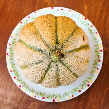 top view of whole sicilian muskmelon (cantaloupe melon) on plate on wooden table