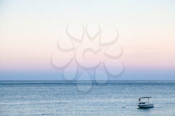 travel to Sicily, Italy - one boat on blue water of Ionian sea near Giardini Naxos town in blue and pink summer twilight