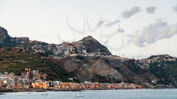 travel to Sicily, Italy - view of Giardini Naxos town below and Taormina city above on cape in summer evening