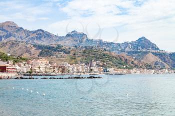 travel to Sicily, Italy - Ionian sea near waterfront of Giardini Naxos town and view of Taormina city on cape in summer