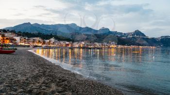 travel to Sicily, Italy - urban beach in Giardini Naxos town and view of Taormina city on cape in summer evening