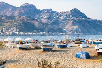 travel to Sicily, Italy - ships on beach in old port in Giardini Naxos town and view of Taormina city on cape in summer