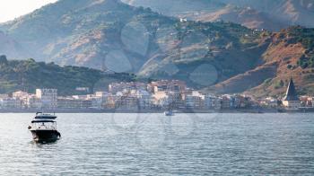 travel to Sicily, Italy - boat in Ionian Sea and view of Giardini Naxos town in summer evening