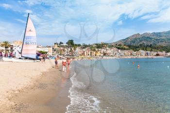 GIARDINI NAXOS, ITALY - JUNE 28, 2017: tourists and boats on beach near waterfront of Giardini-Naxos town. Giardini Naxos is seaside resort on Ionian Sea coast since the 1970s