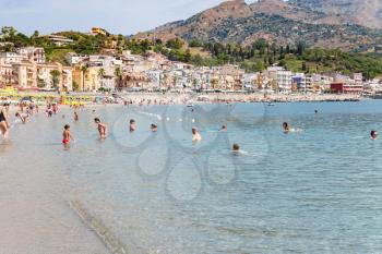 GIARDINI NAXOS, ITALY - JUNE 28, 2017: Vacationers on beach near waterfront of Giardini-Naxos town. Giardini Naxos is seaside resort on Ionian Sea coast since the 1970s
