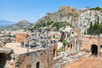 TAORMINA, ITALY - JUNE 29, 2017: tourists in Teatro antico, ancient Greek Theater (Teatro Greco) and view of Taormina city on mountain slope. The amphitheater was built in the third century BC