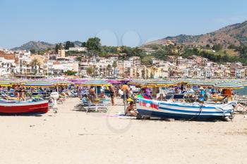 GIARDINI NAXOS, ITALY - JUNE 30, 2017: tourists and boats on beach in Giardini-Naxos city in summer. Giardini Naxos is seaside resort on Ionian Sea coast since the 1970s