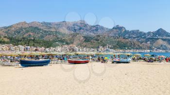 GIARDINI NAXOS, ITALY - JUNE 30, 2017: people and boats on beach in Giardini-Naxos city in summer. Giardini Naxos is seaside resort on Ionian Sea coast since the 1970s