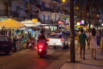 GIARDINI NAXOS, ITALY - JUNE 28, 2017: tourists, shops and car traffic on waterfront in Giardini-Naxos town in summer night. Giardini Naxos is seaside resort on Ionian Sea coast since the 1970s