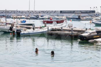 GIARDINI NAXOS, ITALY - JUNE 30, 2017: people swim in sea in urban port of Giardini-Naxos city in summer. Giardini Naxos is seaside resort on Ionian Sea coast since the 1970s