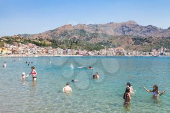 GIARDINI NAXOS, ITALY - JUNE 30, 2017: people in Ionian Sea on urban beach in Giardini-Naxos city in summer. Giardini Naxos is seaside resort on Ionian Sea coast since the 1970s