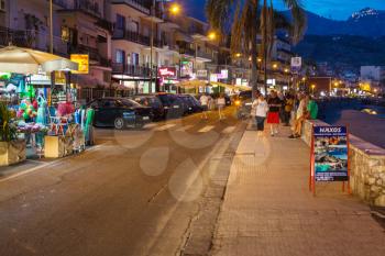 GIARDINI NAXOS, ITALY - JUNE 28, 2017: tourists near gift shops on waterfront in Giardini-Naxos town in summer night. Giardini Naxos is seaside resort on Ionian Sea coast since the 1970s