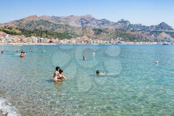 GIARDINI NAXOS, ITALY - JUNE 30, 2017: tourists in Ionian Sea on urban beach in Giardini-Naxos city in summer. Giardini Naxos is seaside resort on Ionian Sea coast since the 1970s