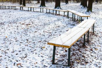 wooden benches covered with the first snow in recreation area of urban park in frosty autumn day