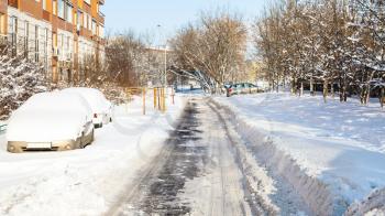 snow-covered cars along urban road in residential district of Moscow city in sunny winter day