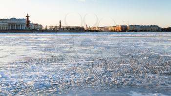 view of frozen Neva river and Spit of Vasilyevsky Island with Rostral Column and Old Stock Exchange building in Saint Petersburg city in March evening