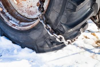 Snow chain fitted to tractor tire on snow-covered road close up