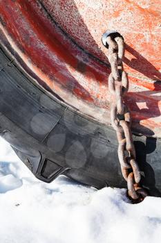 rusty snow chain fitted to tractor wheel on snow-covered road close up