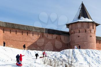 people on snow slope of riverbank near wall of Monastery of Our Savior and St Euthymius in Suzdal town in winter in Vladimir oblast of Russia