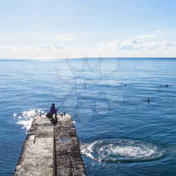 travel to Crimea - fisher on pier and swimming tourists in Black Sea in Alushta city in morning