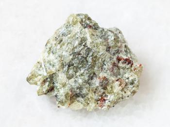 macro shooting of natural mineral rock specimen - raw olivine stone on white marble background from Kovdor region, Kola Peninsula, Russia
