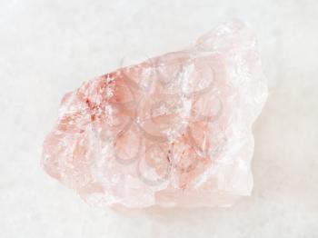 macro shooting of natural mineral rock specimen - rough crystal of rose quartz gemstone on white marble background from Kiv-Guba mine, Karelia, Russia