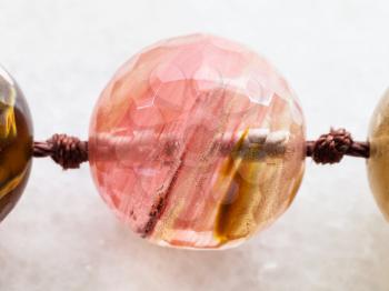 macro shooting of natural mineral rock specimen - bead from rose quartz gemstones on white marble background