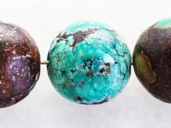 macro shooting of natural mineral rock specimen - beads from Turquoise gemstone on white marble background