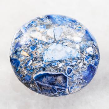 macro shooting of mineral rock specimen - bead from artificial pressed Lazurite stone on white marble background