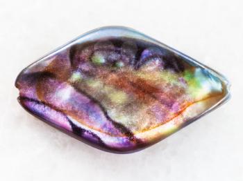 macro shooting of natural mineral rock specimen - bead from Abalone (haliotis) shell on white marble background