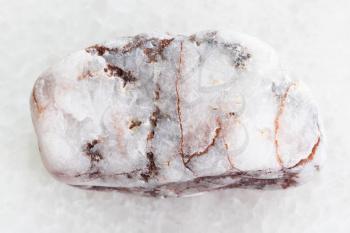 macro shooting of natural mineral rock specimen - tumbled marble gem on white marble background from Greece