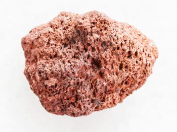 macro shooting of natural mineral rock specimen - tumbled red pumice pebble on white marble background from Sicily