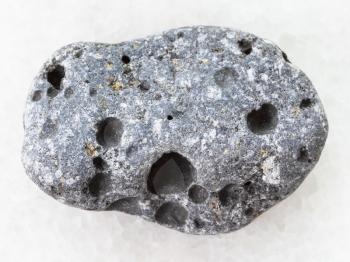 macro shooting of natural mineral rock specimen - tumbled gray pumice stone on white marble background from Sicily