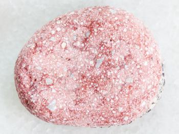 macro shooting of natural mineral rock specimen - pebble of pink Arkose sandstone on white marble background