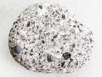 macro shooting of natural mineral rock specimen - pebble of gray Arkose sandstone on white marble background