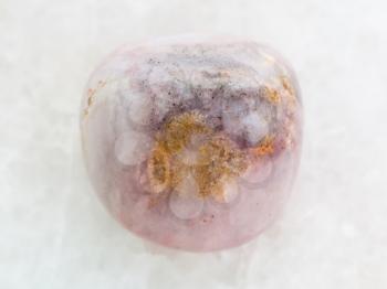 macro shooting of natural mineral rock specimen - polished rhodonite gem stone on white marble background